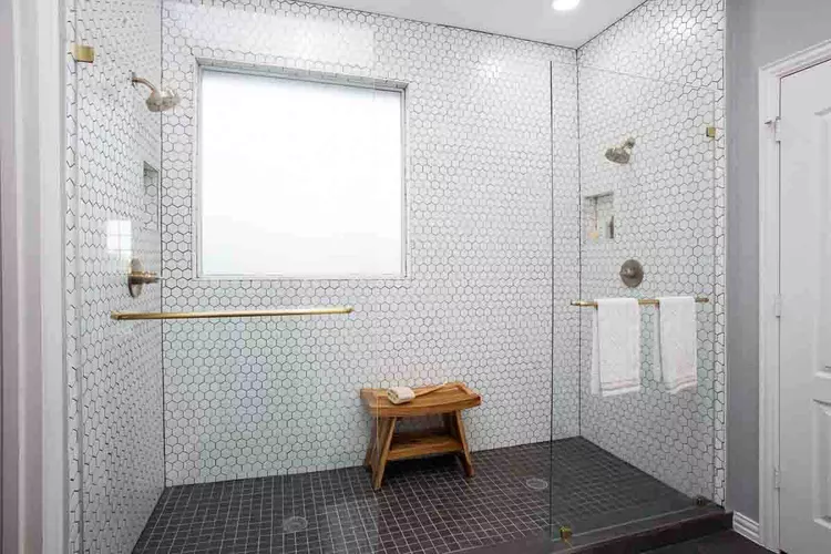 Walk-in shower with white hex tile walls, glass panel and dark mosaic floor