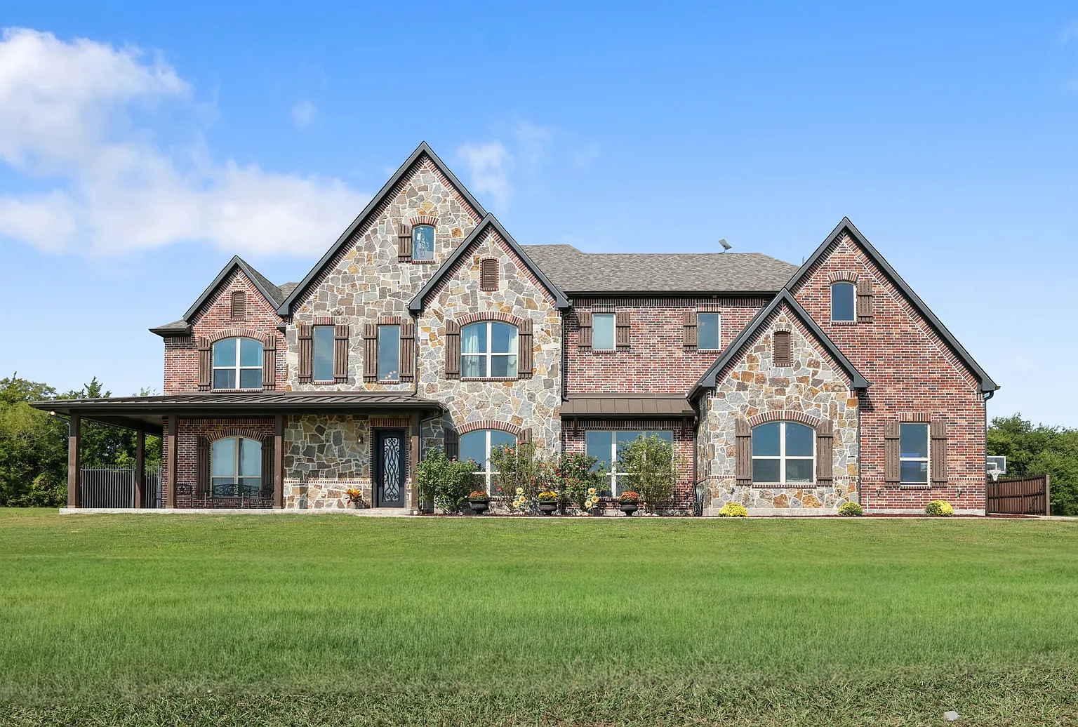 Two-story brick and stone home with a covered porch on a wide lawn