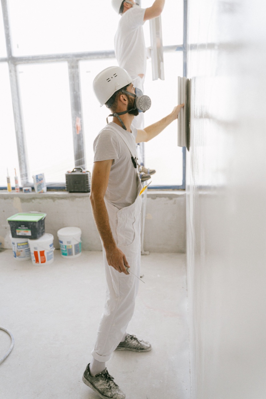 Drywall finisher in a respirator smoothing a freshly skimmed wall